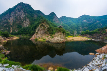 Fototapeta premium Traditional Korean pavilion Wollyujeong perched on a rocky hill by the river with perfect water reflection and scenic mountain backdrop, Yeongdong, South Korea.