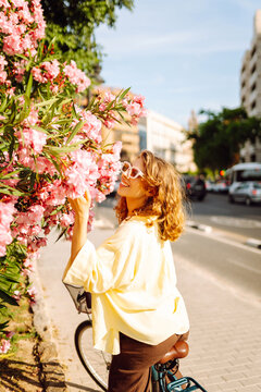 A happy woman is cycling through a sunny city surrounded by blossoming trees. A woman with a bicycle is enjoying a sunny day outdoors. Concept of relaxation, enjoyment.