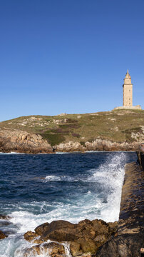Waves crashing against rocks with the Tower of Hercules in the background