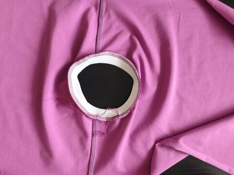 Finished overlock stitch on a white knit neckline of a purple jersey tank top, garment assembly step, close-up top view.