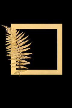 Gold fern leaf frond floral border isolated on black background with gold frame. Nature minimal zen design symbol for decorative purposes for greeting card.
