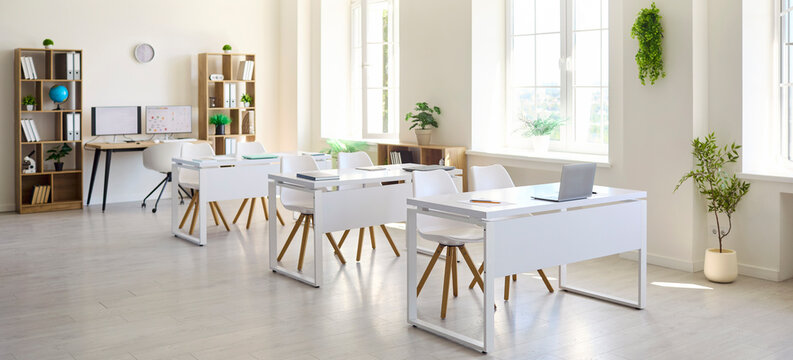 Modern classroom interior with empty desks for education. Sunlit room with white furniture and laptops for school use, training and workshops. Clean bright learning space concept for education.