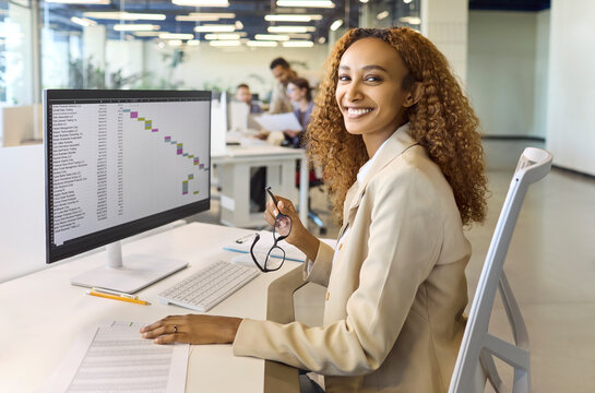 Analyst businesswoman reviews finance data on computer. In a bright office she studies charts and report on a large monitor. The portrait suits corporate uses. Clear data driven finance concept.