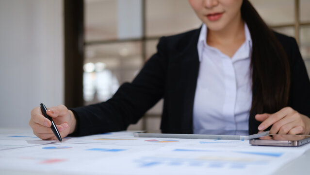 Businesswoman writing notes while reviewing financial charts and reports on an office desk.