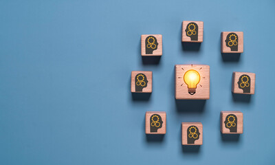 Fototapeta premium Wooden blocks with human head icons surrounding a glowing light bulb, symbolize teamwork, innovation, brainstorming, creative thinking, knowledge sharing, problem solving and business collaboration.
