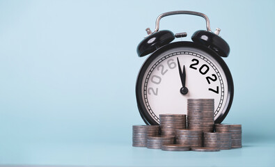 Alarm clock with stacked coins and 2026 to 2027 transition new year for symbolize financial planning, savings, investment growth, budgeting, retirement goals and wealth management.