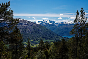 Obraz premium Norwegian mountain vista: snow peaks, lush valley, blue lake, vibrant pine trees