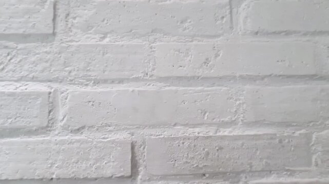 Moving background of traditional white-painted brick wall texture, up close. Surface of rough-textured brick wall painted with visible mortar lines, for a modern industrial or rustic minimalist decor.