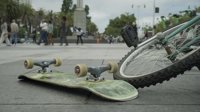 Skateboard and Bicycle Lying on Pavement Ground Level In San Francisco Plaza With Man Doing Tricks With Painted Board In Distance