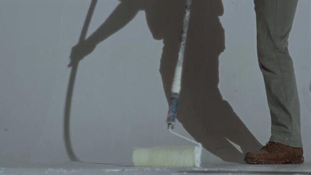 A worker paints the floor of a cyclorama in the room of a photo studio with white paint