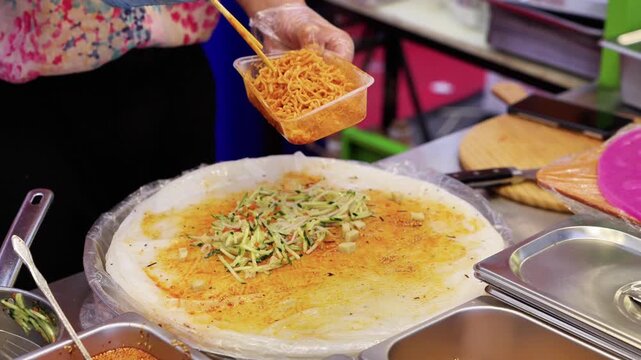 A food vendor adds spicy noodles to a large flatbread for making street-style wraps at a stall.
