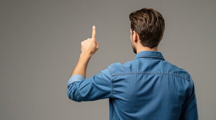 Naklejka premium Man in denim shirt points finger up. Back view of person indicating choice or idea, perhaps making a selection or offering guidance. Casual gesture, focused on action.