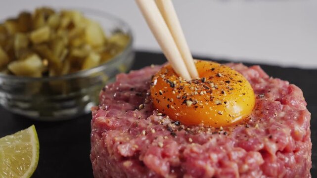 Raw beef tartare with sauce on a black stone tray. Homemade tartare with onion, capers, and egg yolk. High-quality 4K video. High quality 4k footage