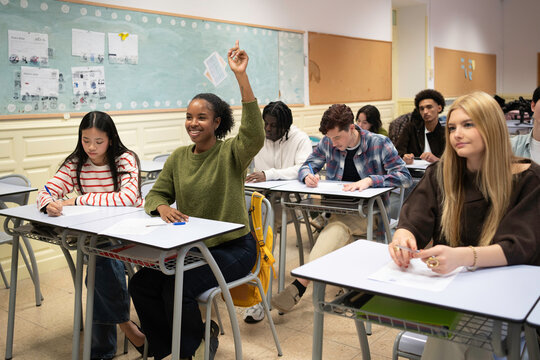 Young black female student raising hand in a classroom full of diverse college students