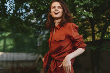 Naklejka premium Smiling woman in a red shirt outdoors, casual lifestyle portrait among green trees, warm sunlight, candid moment, fresh air, relaxed mood for lifestyle and outdoor living vibes