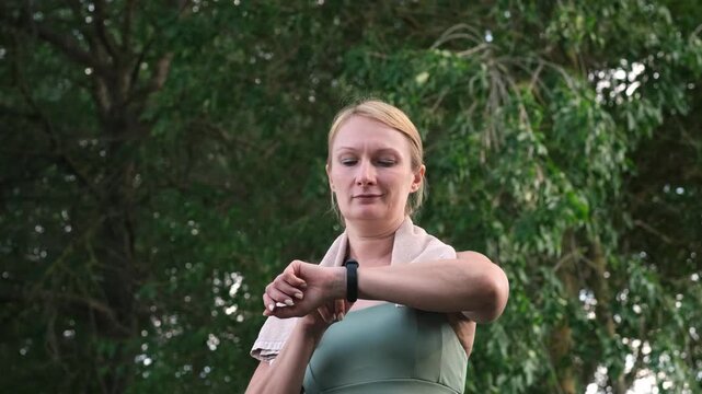 Woman in sportswear checking heart rate on fitness tracker in morning park. Concept of health monitoring and regular exercise routine