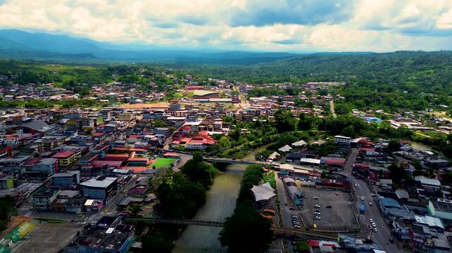Aerial View of Tropical Ecuador Town with River, Bridge, Green Hills, Urban Buildings and Cloudy Sky, South American Cityscape Travel Scene