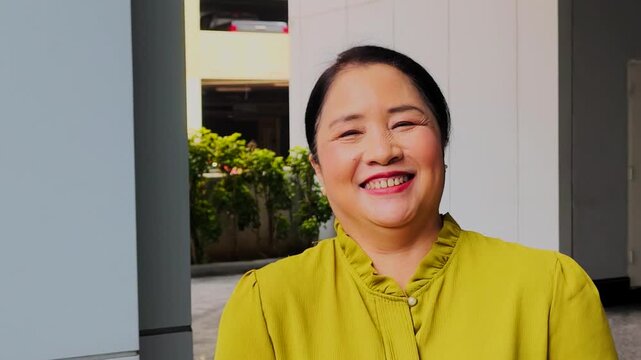 Relaxed happy smiling old senior asian woman in her 50s with positive friendly face expression in healthy green urban environment