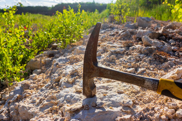 Close-up of a weathered steel geological rock hammer resting on raw limestone at an open-pit quarry during an amateur expedition to discover ancient fossils and mineral samples © PhotoChur