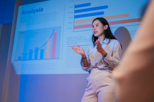 A young businesswoman gestures confidently while presenting a financial analysis slide with growth charts and plan comparisons, illustrating a professional data presentation session
