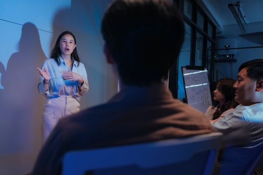 A young businesswoman gestures confidently while presenting a financial analysis slide with growth charts and plan comparisons, illustrating a professional data presentation session