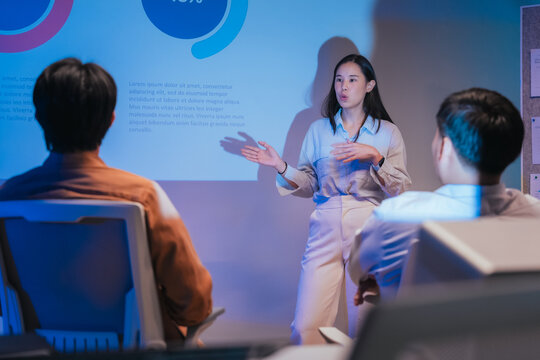A young businesswoman gestures confidently while presenting a financial analysis slide with growth charts and plan comparisons, illustrating a professional data presentation session