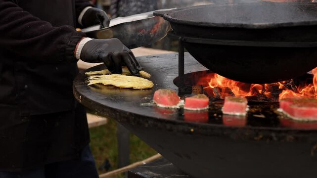 Raw fish steak cooking on a rustic metal fire pit. Salmon fillet grilling over open flames in outdoor kitchen. Culinary process of preparation fresh seafood.