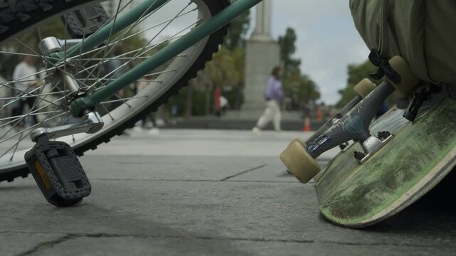 Bicycle Pedal and Skateboard Upright Against Wheel In San Francisco Plaza With Crowds