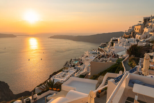A serene sunset view from Imerovigli, Santorini, overlooking the iconic caldera and the Aegean Sea. Warm golden‑hour light illuminates the whitewashed Cycladic architecture,  and dramatic cliffs.