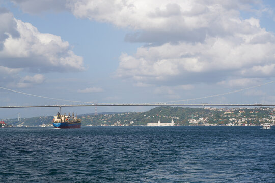 Iconic 15 Temmuz Şehitler K&ouml;pr&uuml;s&uuml; (July 15 Martyrs' Bridge) elegantly arching over the calm Bosphorus in Istanbul, with a cargo ship passing below and the city's green hills in the background.