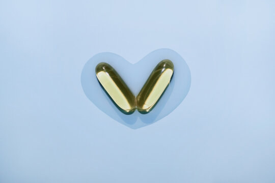 Two fish oil softgels creating heart shape on pastel blue background