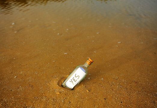Affirmative message in a bottle against a full image background of a saturated dark ochre wet sand. Bottle on the beach, washed ashore by the tide, containing a positive message.