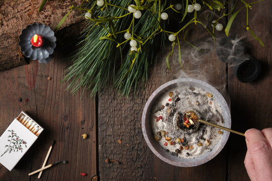 Frankincense and dried herbs burning on glowing charcoal - placing incense with a spoon