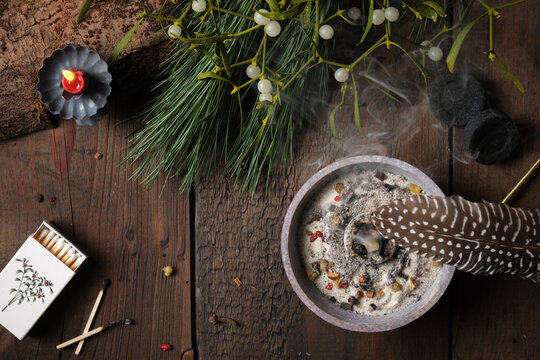 Incense burning on glowing charcoal with dark background - spreading smoke with a feather