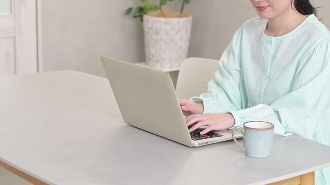 リビングでノートパソコンを使って作業する30代女性の手元