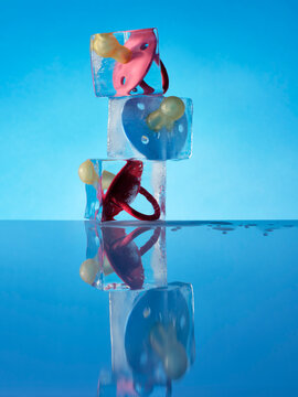 Baby's dummies  frozen in an ice cube against blue