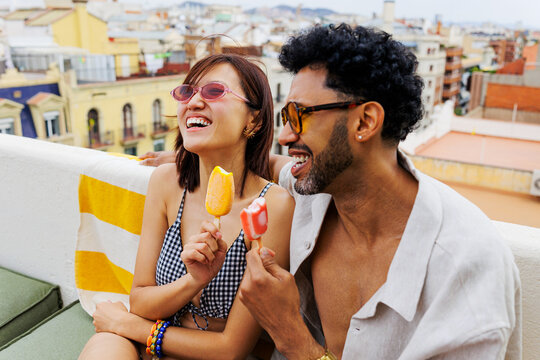 Laughing couple enjoying refreshing ice pops on a rooftop