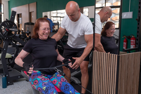Senior woman and personal trainer on rowing machine correcting posture