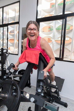 Smiling senior woman performing arm flexion on gym machine