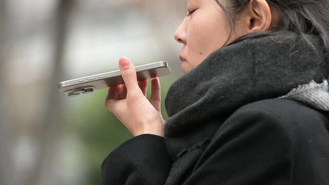 冬の屋外でスマートフォンのスピーカーホンを使う30代の日本人女性