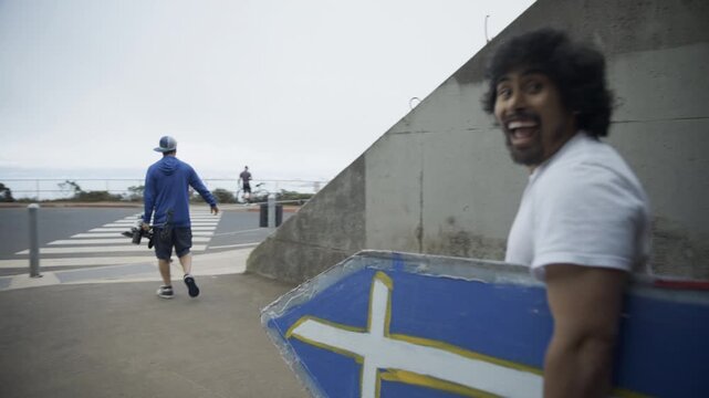 Man Carrying Blue Cross Board Toward Coastal Parking Lot  - Wide Shot
