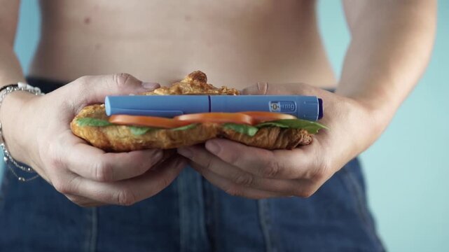 a person holding a sandwich made of a croissant with a weight loss injection pen inside it on a light blue background the subject is not visible from the face focused on the medication and food concep