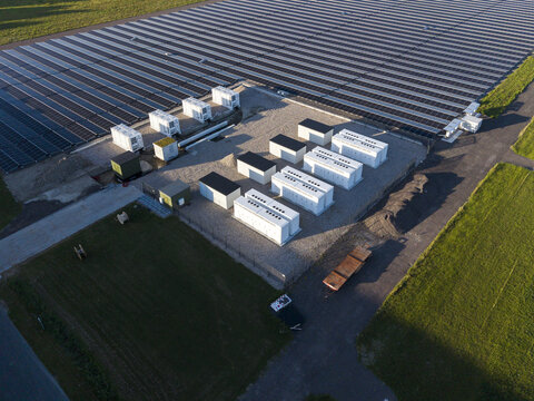 Aerial view of a solar farm featuring rows of photovoltaic panels and white battery energy storage containers in a rural landscape in Middenmeer, North Holland, Netherlands.