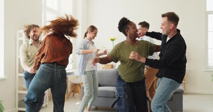 Friends group of young adults dancing at home. Lively indoor party in a bright living room with smiles, fun and motion for lifestyle ads. Joyful friendship, celebration and carefree home vibes.