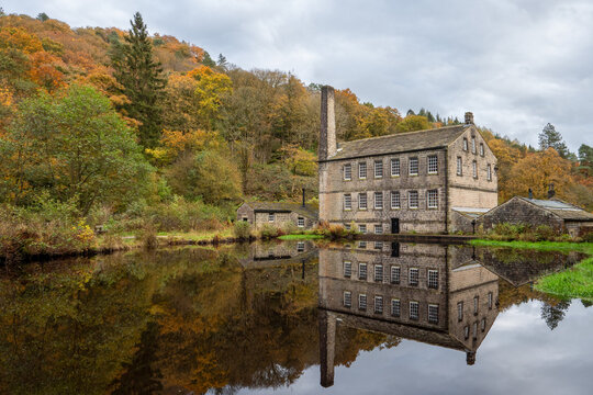 Gibson Mill a historic cotton mill dating from the early 19th century reflected in the mill pond and surrounded by the autumn woodland of Hardcastle Crags