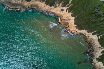 Obraz premium Rugged rocky coast with vibrant turquoise water and green pine trees on the shore, perfect as a design template for summer travel.