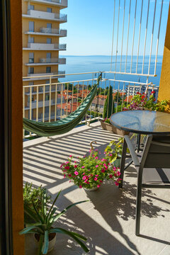 apartment balcony decorated with blooming flowers, a hammock and outdoor furniture overlooking the peaceful Adriatic coastline. Ideal representation of slow travel, summer getaway, wellness lifestyle
