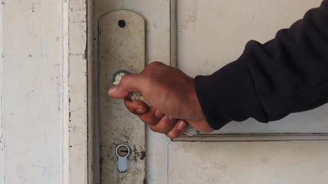 Close-up of a hand carefully opening a weathered wooden door by holding an old door handle. Slow and cautious movement at a rustic entrance.