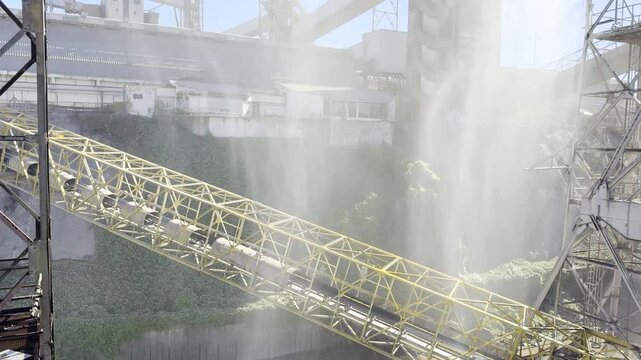 seaport loading facility with conveyors and metal towers. water mist reduces dust from wheat loading to cargo ship. industrial scale and engineering.