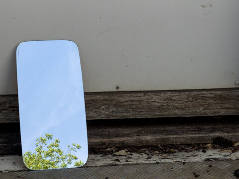 Mirror resting against a weathered wooden door reflecting the blue sky above